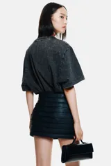 Remera de algodón con efecto acid wash en color negro o gris oscuro, corte oversize y cuello redondo acanalado con argollas metálicas decorativas.