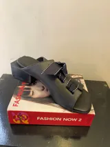 Sandalias negras de cuero sintético con tacón bloque y detalle de moños con pespuntes blancos en el empeine.