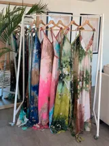 Vestido largo de tela fluida, color verde esmeralda con estampado abstracto en tonos turquesa y detalles dorados. Diseño asimétrico con un solo tirante tejido en el hombro.