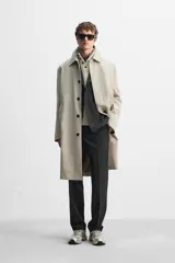 Gabardina color beige de corte relaxed fit, confeccionada en tejido italiano repelente al agua. Tiene cuello solapa, manga larga con puños abotonados, bolsillos de vivo en la cadera, bolsillo interior y abertura en la espalda.