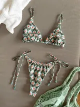 Traje de baño de dos piezas con estampado floral en tonos celeste, blanco y verde. El corpiño es de corte triangular con tirantes finos y detalle de cuentas en los tirantes. La bombacha es de corte clásico con tiras laterales ajustables.