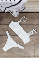 Conjunto de bikini blanco con textura acanalada, compuesto por un corpiño bandeau con breteles regulables y lazo en la espalda, y una bombacha vedetina con frunce elástico en los costados.