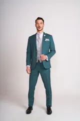 Traje de ceremonia color verde esmeralda, compuesto por saco, pantalón y chaleco. El saco es de corte clásico, con solapa de muesca, dos botones y bolsillos con solapa. El pantalón es de corte recto, con cierre y bolsillos laterales. El chaleco es de color gris plata con diseño de cachemira.