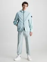 Campera con capucha Calvin Klein, confeccionada en nailon 100% reciclado color celeste. Tiene cierre de cremallera frontal, cuello alto, bolsillos delanteros con cremallera, puños y dobladillo elásticos, tirador de cremallera con la marca e insignia con el logo de Calvin Klein en la manga.