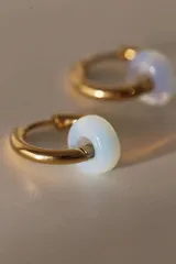 Par de aros tipo argolla dorados con dije de piedra natural con patrón de manchas negras sobre fondo blanco.