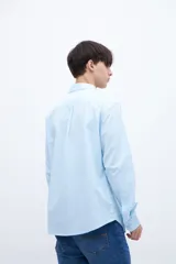 Camisa celeste de algodón, corte regular fit, con cuello solapa clásico, manga larga, bolsillo en el pecho y botones personalizados.