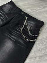 Pantalón de jean negro con lavado gastado, corte ancho y cadena metálica colgando del bolsillo.