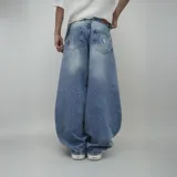 Jean de hombre, color celeste desgastado, corte ultra ancho (baggy) y tiro alto. Presenta un parche de cuero marrón con logo en el reverso de la cintura y un estampado circular blanco en el bolsillo trasero derecho.