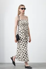 Vestido midi de silueta fluida con estampado de grandes lunares negros sobre fondo beige. Cuenta con un cuerpo fruncido elástico tipo nido de abeja, escote recto y tirantes finos regulables que se anudan en los hombros.