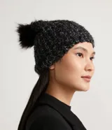 Gorro de lana negro con textura de punto trenzado y pompón de piel sintética en la parte superior.