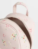 Mochila pequeña de cuerina color crema con estampado de flores pequeñas en tonos rosa, naranja y celeste. Tiene un bolsillo frontal con cierre, correas regulables, manija superior, cierre superior y bolsillos laterales.