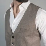 Chaleco de vestir marrón claro con textura de espiga, cuello en V, cierre frontal con botones y bolsillos ribeteados.