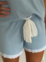 Conjunto de pijama de dos piezas color negro, compuesto por una remera de manga corta con escote en V adornado con puntilla beige, y un short con lazo frontal beige y terminación de puntilla beige en el ruedo.