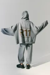 Buzo gris de frisa con capucha, bolsillos delanteros y corte oversize. Tiene recortes laterales, doble cordón con puntera de goma y estampa en frente y espalda.