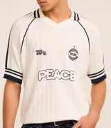 Camisa polo de punto color blanco con rayas azul marino en cuello y mangas. Tiene bordados localizados y lettering.