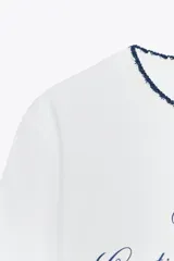 Camiseta blanca de algodón con cuello redondo y detalle de tricot a contraste en azul marino. Estampado frontal con texto "Estate sulla Costiera Amalfitana" en azul marino.