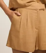 Short corto color beige confeccionado en viscosa y lino, con cierre lateral desplazado, pliegues delanteros y bolsillos laterales.