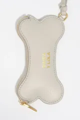 Monedero pequeño con forma de hueso, color gris claro, con cierre de cremallera dorada y correa de mano a juego. Presenta el logo de la marca estampado en dorado en el centro.