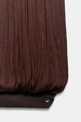 Mono de mujer color marrón oscuro, con escote redondo y tirantes finos. El tejido es satinado y plisado verticalmente. El pantalón es estilo bombacho con bajo abullonado ajustado con botón.