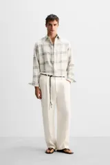 Pantalón color crema de lino, corte amplio, con pliegues frontales, bolsillos laterales y traseros de ojal. Cierre frontal con cremallera y gancho metálico oculto.