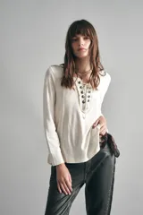 Remera negra de algodón con calce relajado, cuello redondo y mangas largas. Presenta una abertura frontal con arandelas metálicas y cordón.
