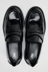 Mocasín negro de charol con detalle de antifaz en el empeine y punta redonda.
