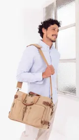 Mochila de tela canvas color beige con detalles en cuero marrón. Cuenta con múltiples bolsillos con cierre, compartimento acolchado para notebook y correas ajustables.