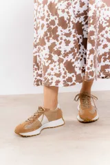 Zapatillas deportivas color beige con detalles metalizados dorados, confeccionadas en cuero con perforaciones, cordones ajustables y suela de goma dentada.