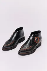 Botín acordonado de cuero marrón con textura grabada y hebilla lateral. Tiene suela de goma negra y puntera redondeada con costuras decorativas.