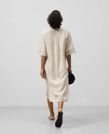 Vestido largo de lino color crema con finas rayas verticales. Tiene cuello mao, mangas cortas anchas, botonadura frontal oculta y un bolsillo en el pecho.