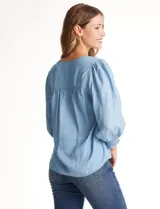 Blusa de lyocell color azul claro, con escote en V, detalles de costuras verticales en el frente y mangas tres cuartos con puños elastizados.