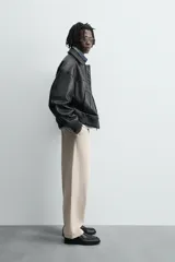 Pantalón chino color beige, de corte relaxed fit, confeccionado en tejido de mezcla de algodón y lino. Cuenta con bolsillos delanteros y traseros de vivo. Cierre frontal con cremallera y botón.