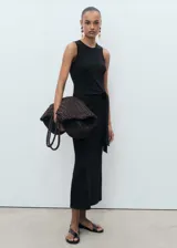 Vestido midi negro, sin mangas, con cuello redondo y tirantes anchos. Presenta un nudo decorativo en la cintura que cae como un lazo.