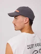 Gorra gris de poliéster y elastano con visera curva y logo de la marca Rusty en color naranja.