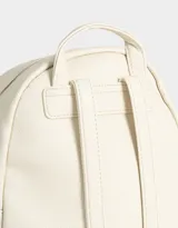 Mochila pequeña de cuerina color rosa pálido, con moño en relieve en el frente y llavero con forma de corazón trenzado. Tiene correas regulables, manija superior, cierre superior, bolsillo frontal con cierre y bolsillos laterales.