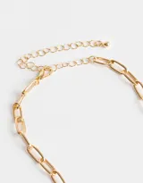 Collar corto dorado con cadena de eslabones grandes y dijes colgantes: corazones dorados, corazón rojo con borde dorado, cruz dorada, perla blanca y dije ovalado negro con detalle de strass.