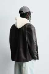 Cazadora de efecto piel color marrón oscuro, corte relajado, con cuello solapa, cierre frontal de botones a presión y bolsillos de vivo en cadera.