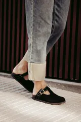 Zuecos negros de cuero con hebilla dorada ajustable.