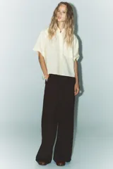 Camisa color crema de cuello solapa y manga corta con vuelta. Tiene un bolsillo de parche en el delantero, bajo asimétrico con aberturas laterales y cierre frontal con botones.