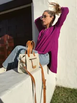 Cartera bandolera de cuero crudo con forro de tela, bolsillo frontal y bolsillo interno. Tiene correa larga regulable y manijas cortas de cuero marrón.