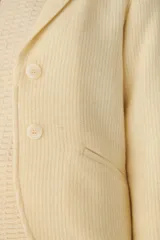 Chaqueta color crema de corte recto con cuello, solapa y bolsillos ojal. Forro solo en las mangas y terminaciones envivadas. Esquinas redondeadas y mangas con corte en puño que permiten transformarla en manga 3/4. Más larga en la espalda que en la delantera. Abrochadura con dos botones.