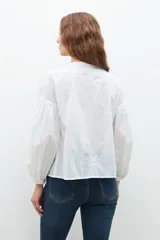 Blusa lila con bordados, de mangas largas abullonadas y cuello en V.