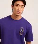 Remera masculina de algodón color violeta, corte comfort, cuello redondo y manga corta. Estampa con dos caras sonrientes en el lateral izquierdo del pecho.