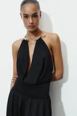 Body blanco de cuello halter con pieza metálica y aplicación joya, escote pico pronunciado, tejido drapeado y cierre inferior con botones a presión.