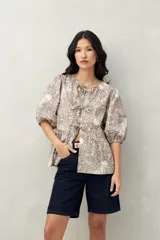 Blusa estampada color beige y blanco, con mangas abullonadas, escote redondo y lazos frontales.