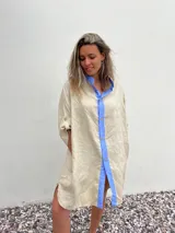 Vestido camisero beige de lino con cuello y solapa azul lavanda, cierre frontal con botones y mangas largas.