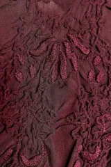 Vestido midi de viscosa color borgoña, con escote en V, tirantes finos ajustables, bordados a tono y volantes en el mismo tejido. El bajo es asimétrico.