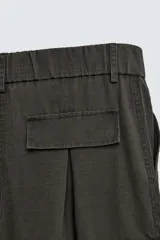 Pantalón cargo de corte ancho y relajado, color verde oscuro o negro, con cintura elástica, bolsillos laterales de parche y bolsillos traseros de vivo. Presenta pliegues verticales marcados en la parte delantera y cordones ajustables en los bajos.