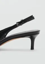 Zapato destalonado negro con punta fina, detalle de flecos y calados, y cierre de hebilla. El tacón mide 5 cm.