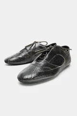 Zapato plano de cuero negro con efecto desgastado y cordones.
